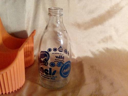 THIS IS AN OLD "NELS" MILK BOTTLE IN THE ORIGINAL ORANGE MILK BOTTLE HOLDER-CRACK IN THE BOTTLE.