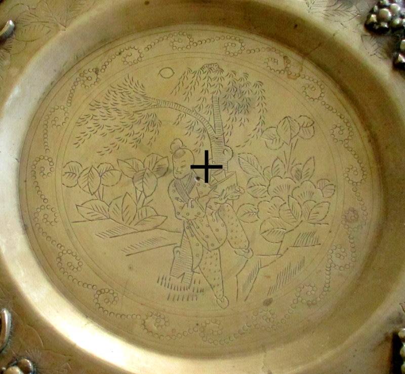 A VINTAGE BRASS PLATE EMBOSSED WITH FRUIT AND ETCHED CENTER ON A STAND