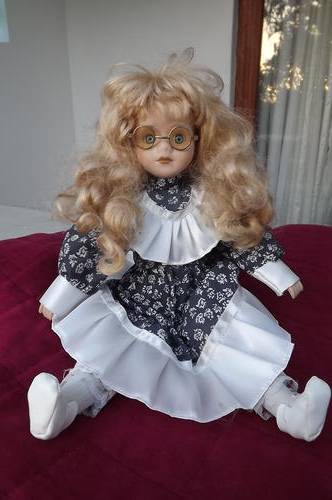 Porcelain blond doll wearing glasses in a navy and white frilled dress and white shoes.
