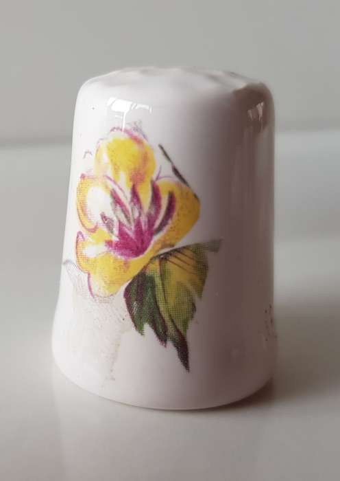 A Vintage collectors thimble. A white ceramic Thimble with painted flower in front.