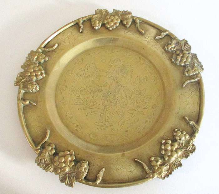 A VINTAGE BRASS PLATE EMBOSSED WITH FRUIT AND ETCHED CENTER ON A STAND