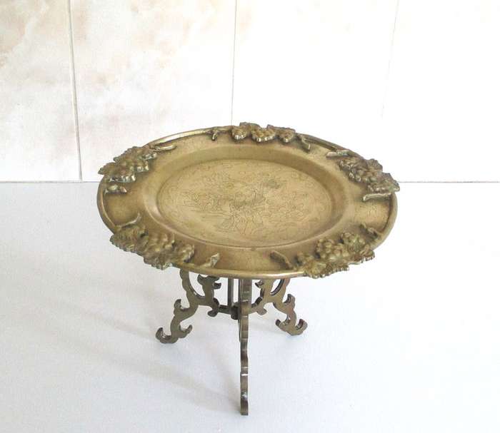 A VINTAGE BRASS PLATE EMBOSSED WITH FRUIT AND ETCHED CENTER ON A STAND