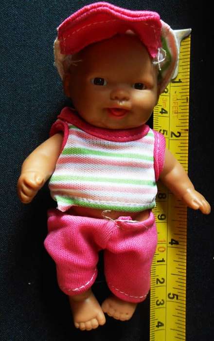 Small light  brown Baby doll in a bright pink utfit with cap. Looks like a Berenguer doll