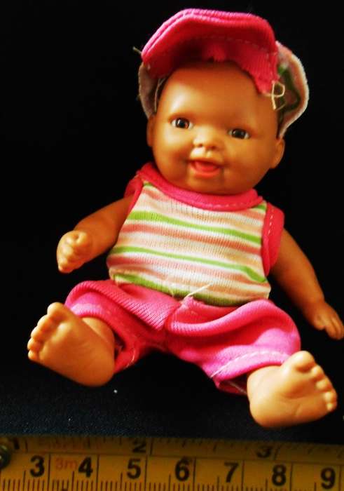 Small light  brown Baby doll in a bright pink utfit with cap. Looks like a Berenguer doll