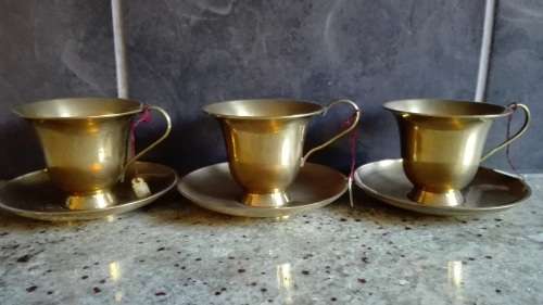 Three solid brass cups and saucers.