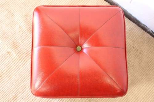 A beautiful, comfy red ottoman with a leather-like upholstery - perfect addition to a living room