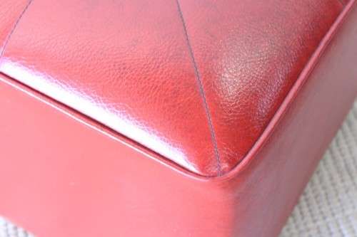 A beautiful, comfy red ottoman with a leather-like upholstery - perfect addition to a living room