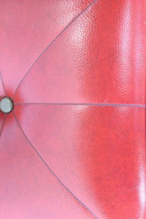 A beautiful, comfy red ottoman with a leather-like upholstery - perfect addition to a living room