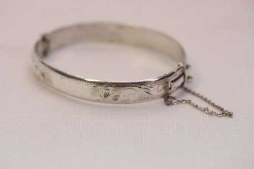 A beautiful vintage hinged sterling silver bangle with floral engraved detailing and a safety chain