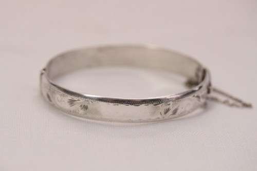 A beautiful vintage hinged sterling silver bangle with floral engraved detailing and a safety chain