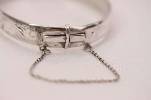 A beautiful vintage hinged sterling silver bangle with floral engraved detailing and a safety chain