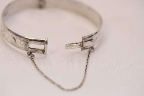A beautiful vintage hinged sterling silver bangle with floral engraved detailing and a safety chain