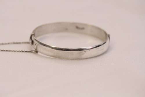 A beautiful vintage hinged sterling silver bangle with floral engraved detailing and a safety chain