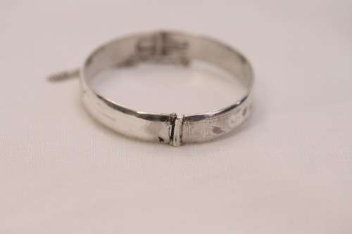 A beautiful vintage hinged sterling silver bangle with floral engraved detailing and a safety chain