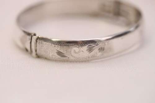 A beautiful vintage hinged sterling silver bangle with floral engraved detailing and a safety chain