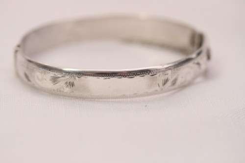 A beautiful vintage hinged sterling silver bangle with floral engraved detailing and a safety chain