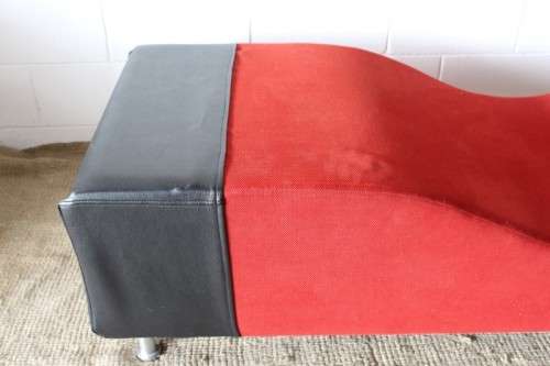 A modern styled black faux leather and red fabric chaise sofa with brushed metal legs