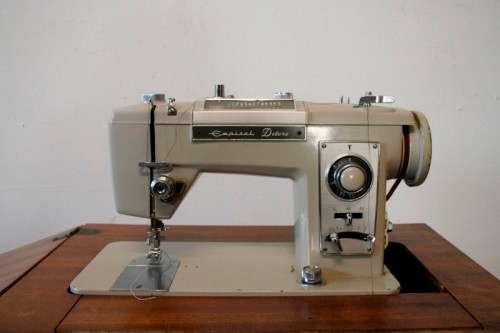 A vintage Empisal deluxe electric sewing machine in its original cabinet w/ accessories, working.