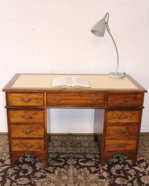 A beautiful vintage knee-hole writing desk w/ an off-white leather top & 9x drawers w/ brass handles