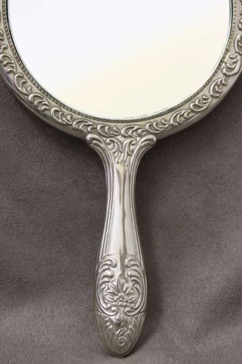 A beautiful, vintage ladies round chrome hand held vanity mirror with lovely detailing on the back.