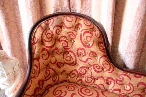 An antique Victorian  "parlour settee" couch w carved detailing and period upholstery on castors.