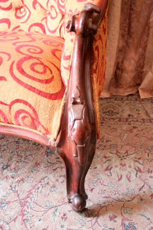 An antique Victorian  "parlour settee" couch w carved detailing and period upholstery on castors.