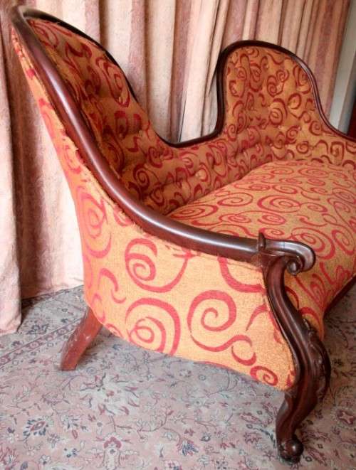 An antique Victorian  "parlour settee" couch w carved detailing and period upholstery on castors.