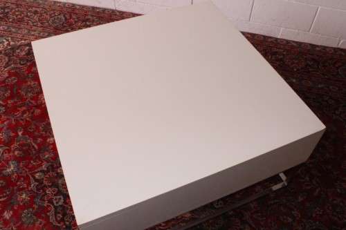 A stunning and modern white square coffee table with a magazine/ book shelf on chromed table legs