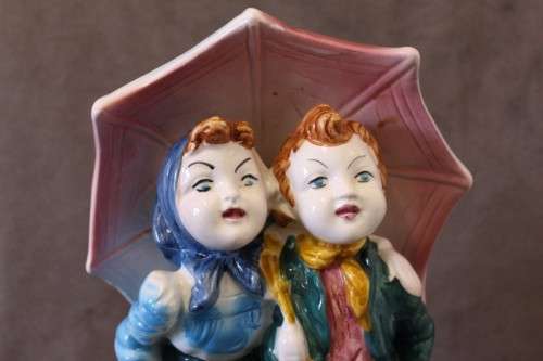 A beautiful porcelain figurine of a young boy and girl under an umbrella, fabulous on display.