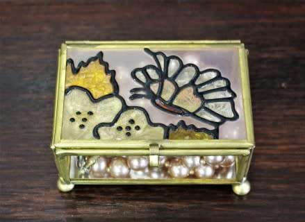 A charming coloured glass trinket box with a gold-coloured frame and mirror base. Lifespace Sale