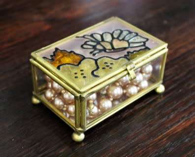 A charming coloured glass trinket box with a gold-coloured frame and mirror base. Lifespace Sale