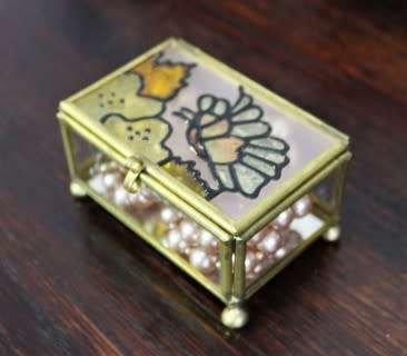 A charming coloured glass trinket box with a gold-coloured frame and mirror base. Lifespace Sale