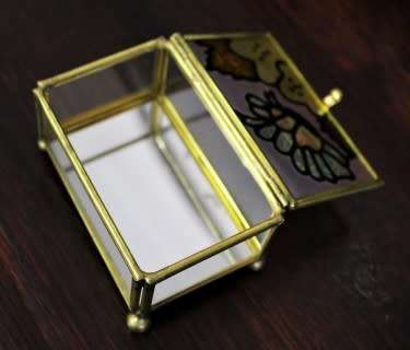 A charming coloured glass trinket box with a gold-coloured frame and mirror base. Lifespace Sale