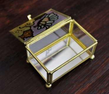 A charming coloured glass trinket box with a gold-coloured frame and mirror base. Lifespace Sale
