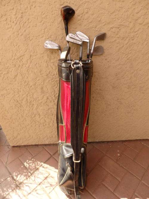 AN AWESOME VINTAGE BLACK AND RED GOLF BAG WITH A MIXED COLLECTION OF IRONS, A WOOD AND A PUTTER