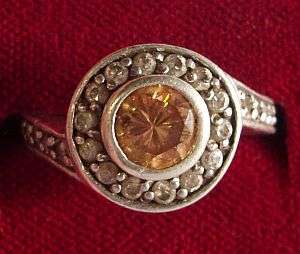 A STERLING SILVER RING SET WITH A FACETED ORANGE GEMSTONE SURROUNDED BY FACETED CZ