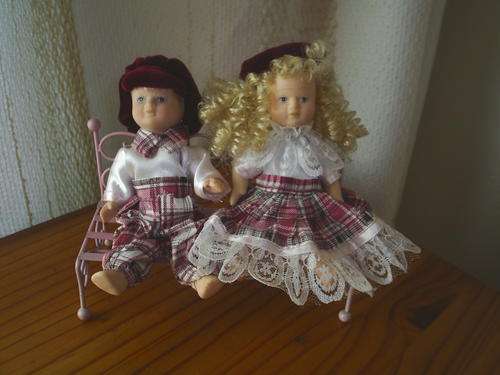 Two Adorable Little Ceramic Dolls Sitting on a Metal Bench