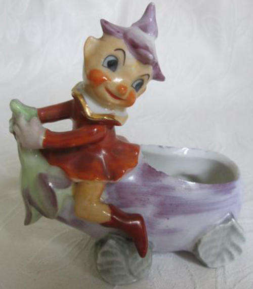 ADORABLE PORCELAIN PIXIE SITTING ON HIS BRINJAL EGG CUP CAR WITH LEAF WHEELS
