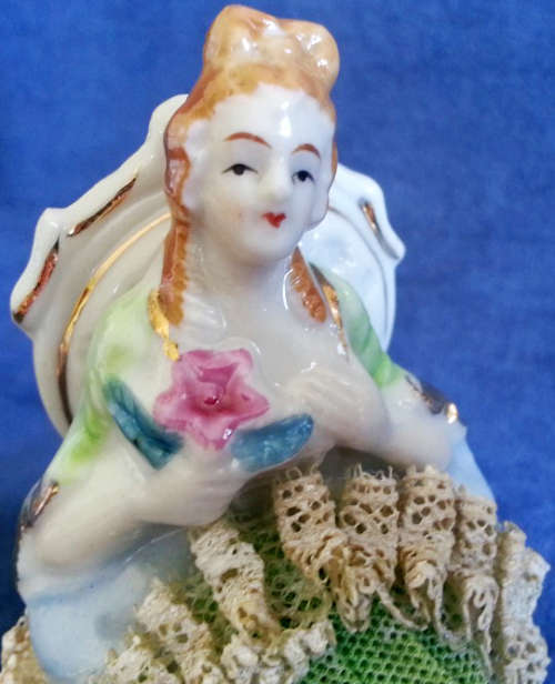 VINTAGE LACE AND PORCELAIN FIGURINE SITTING ON A CHAIR.