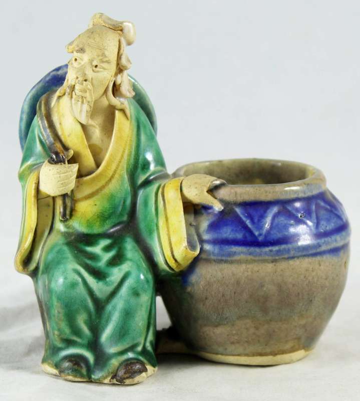 Mud man sitting next to big pot