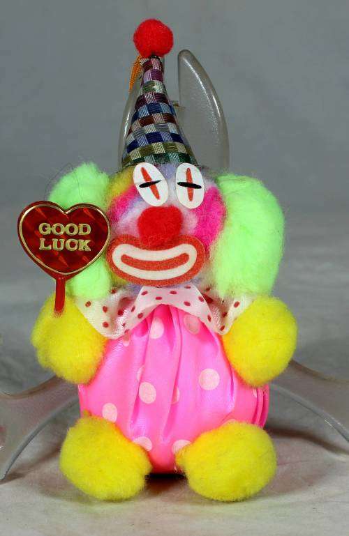 Fuzzy clown dressed in pink holding a good luck sign