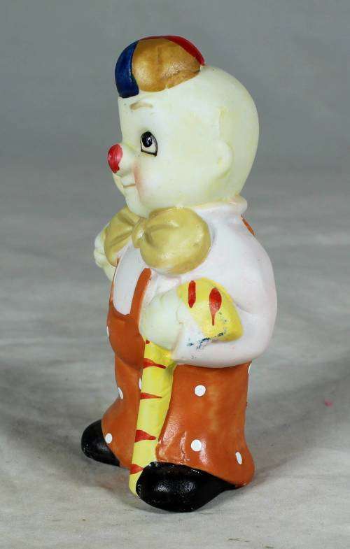 Ceramic clown in an orange jump suite holding a candy cane