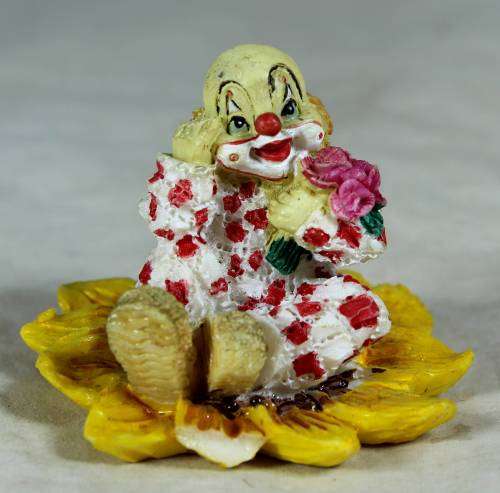 Ceramic clown sitting in a sunflower holding a bunch of roses