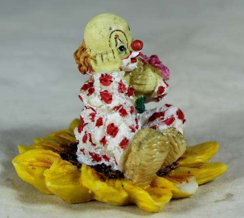 Ceramic clown sitting in a sunflower holding a bunch of roses