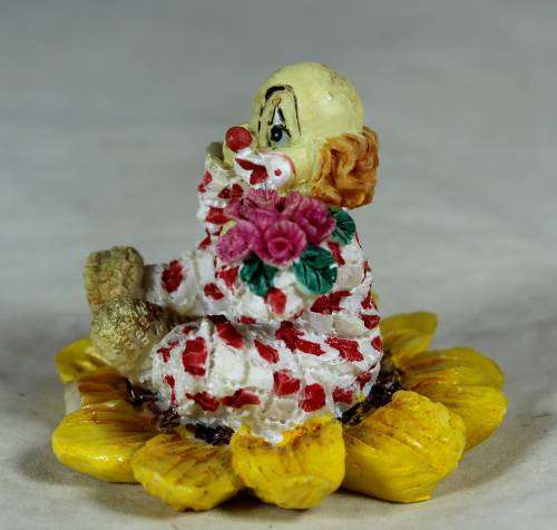 Ceramic clown sitting in a sunflower holding a bunch of roses