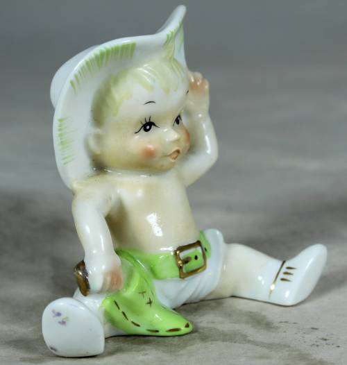 Porcelain sitting cowboy baby with a green gun belt
