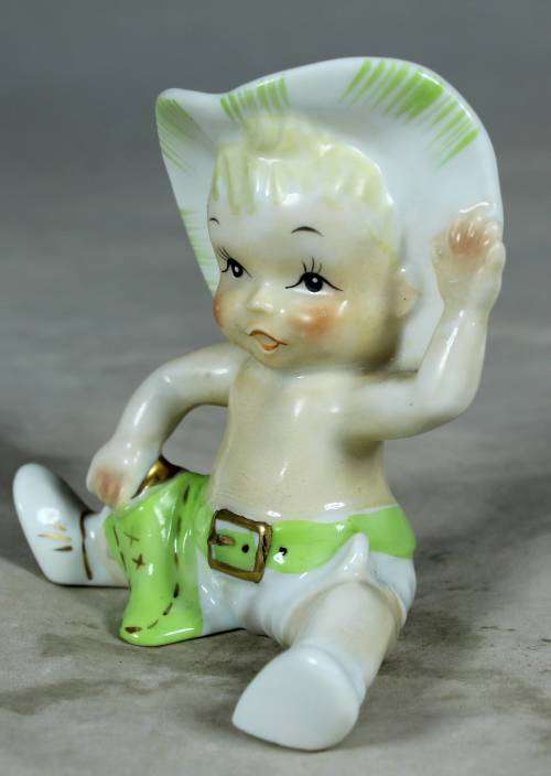 Porcelain sitting cowboy baby with a green gun belt