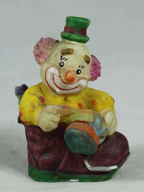 Miniature clown sitting in a shoe polishing his shoe