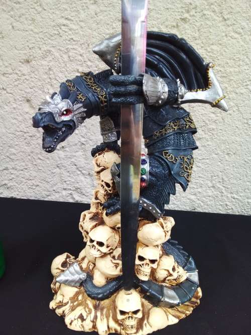 A STUNNING RESIN STATUE OF A DRAGON STANDING ON SKULLS HOLDING A BRASS & STAINLESS SWORD