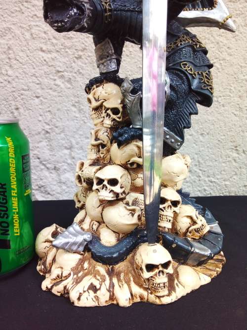 A STUNNING RESIN STATUE OF A DRAGON STANDING ON SKULLS HOLDING A BRASS & STAINLESS SWORD